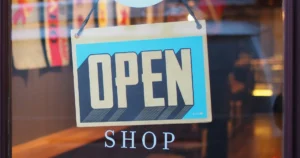 A close-up of an 'Open' sign hanging on the glass door of a shop, reflecting a cozy and inviting interior.